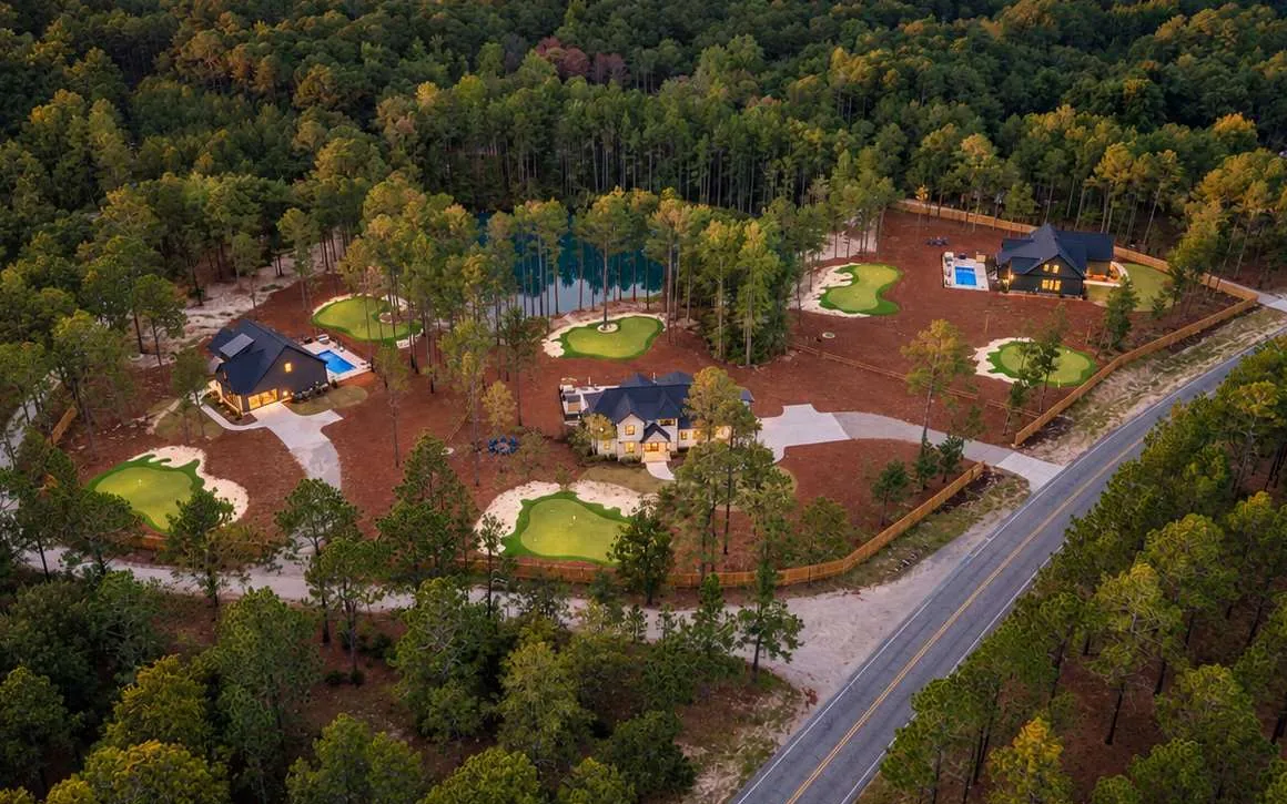 Aerial view of The Aviary at dusk: three houses, pools, and lit putting greens set into the pines